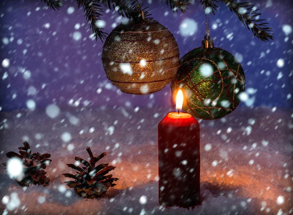 Красная свеча на фоне рождественских украшений и падающего снега — стоковое фото