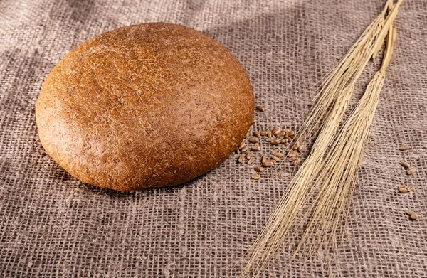 Baked bread, wheat grains and wheat ears on a fabric background — Stock Photo, Image