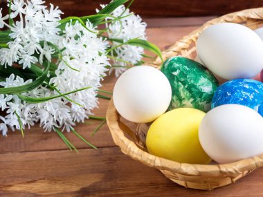 Paskalya yumurtaları ve ahşap arka plan üzerinde beyaz çiçekler ile hasır sepet