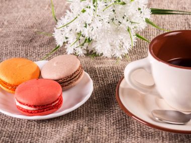Çay ve çiçeklerle ahşap masa üzerinde renkli macarons.