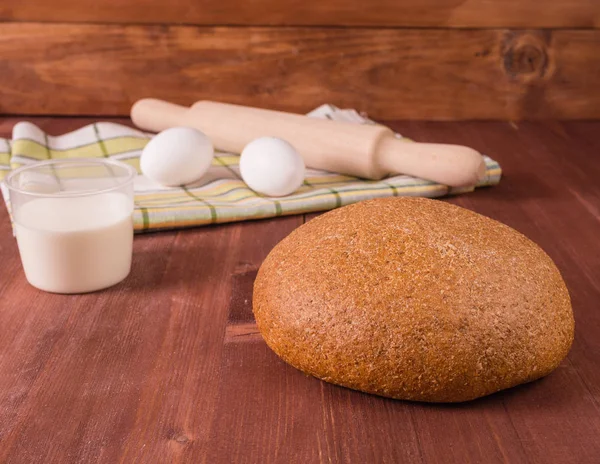 Bread and milk on a wooden table and a basket of bread and eggs on a tablecloth — Stock Photo, Image