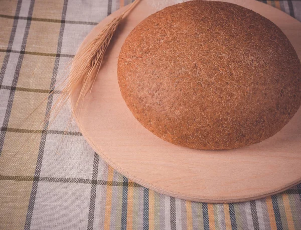 Round bread on a wooden tray and ears of wheat — Stock Photo, Image