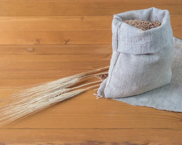 Saco de trigo e orelhas sobre um fundo de madeira — Fotografia de Stock