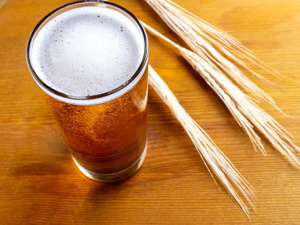 Kufelek piwa z pszenicy uszy na drewnianym stole — Zdjęcie stockowe