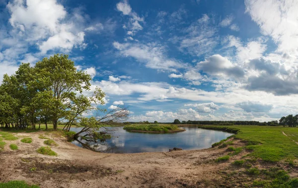 Eine herrliche panoramische Sommerlandschaft mit einem Fischer, einem Fluss und einem schönen wolkenverhangenen Himmel. Das Flussufer, bedeckt mit grünem jungen Gras und einem einsamen Fischer. Das Ende des Frühlings, der Anfang des Sommers — Stockfoto