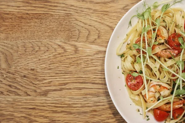 yarısı beyaz bir tabak karides scampi ve üst görünümden ahşap bir masa üzerinde linguine ile