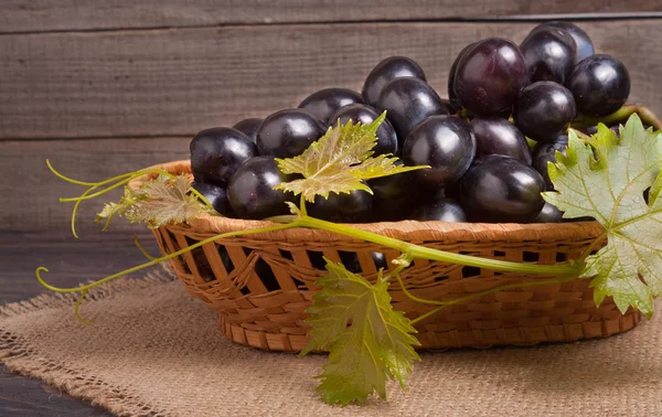 Синий виноград в плетеной корзине на деревянном столе — стоковое фото