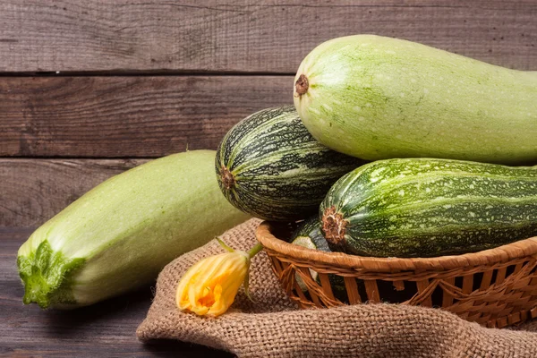 Green zucchini and courgettes with a flower on sackcloth wooden background — Stock Photo, Image