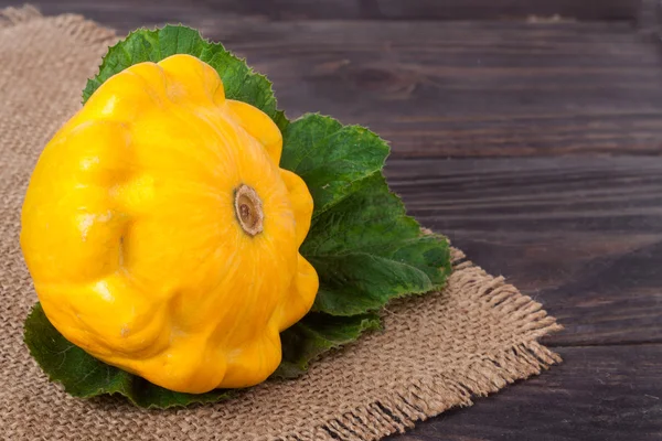 Una calabaza amarilla sobre un fondo de madera con servilleta de arpillera —  Fotos de Stock