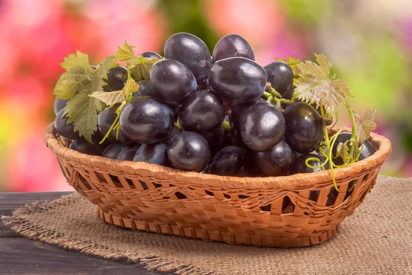 Синий виноград в плетеной корзине на деревянном столе с размытым фоном — стоковое фото
