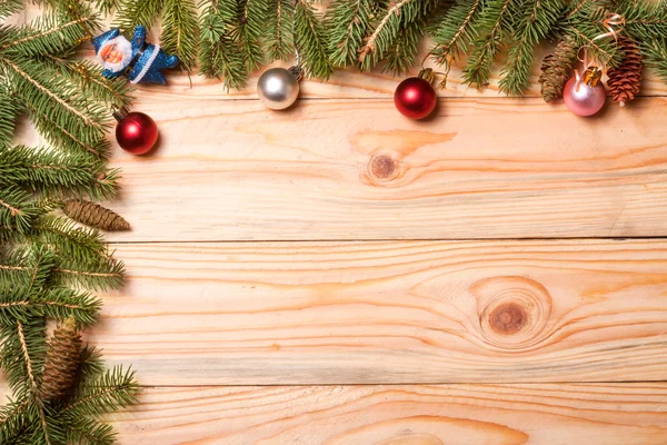 Corner frame of fir branches with Christmas decorations on a light wooden background