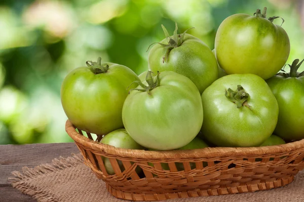 Tomates verdes inmaduros en una canasta de mimbre sobre una mesa de madera con fondo borroso — Foto de Stock