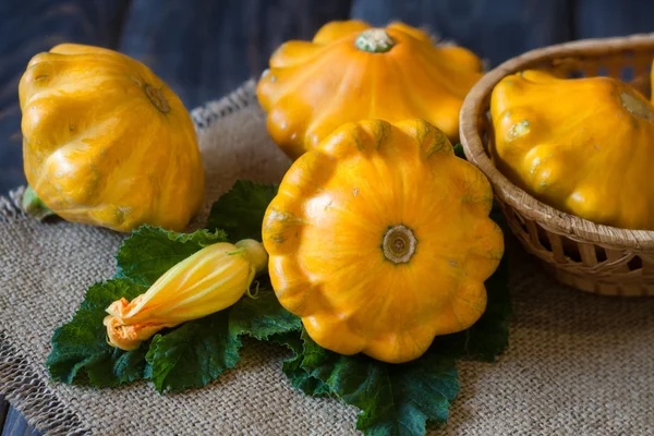 Tres calabaza pattypan amarillo con hoja y flor en una mesa de madera oscura —  Fotos de Stock