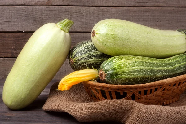 Green zucchini and courgettes with a flower on sackcloth wooden background — Stock Photo, Image