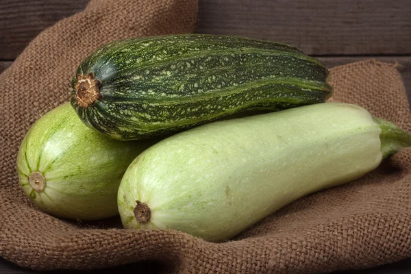 Grüne Zucchini und Zucchini auf Sacktuch hölzernen Hintergrund — Stockfoto