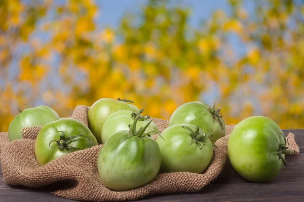 Tomates verdes imaturos em pano de saco e mesa de madeira com fundo embaçado — Fotografia de Stock