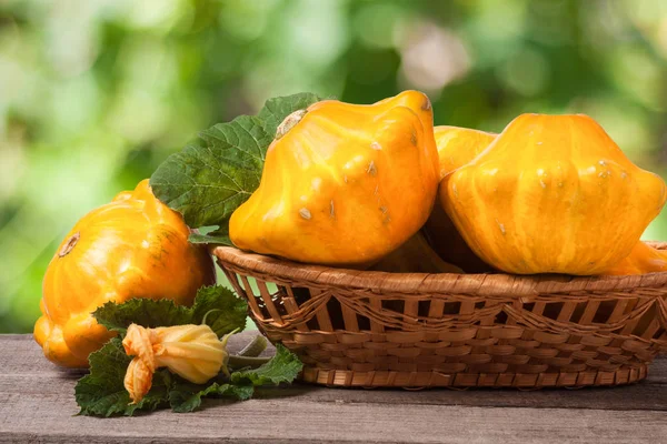 Yellow pattypan squash with leaf in a wicker basket on wooden table blurred background — Stock Photo, Image