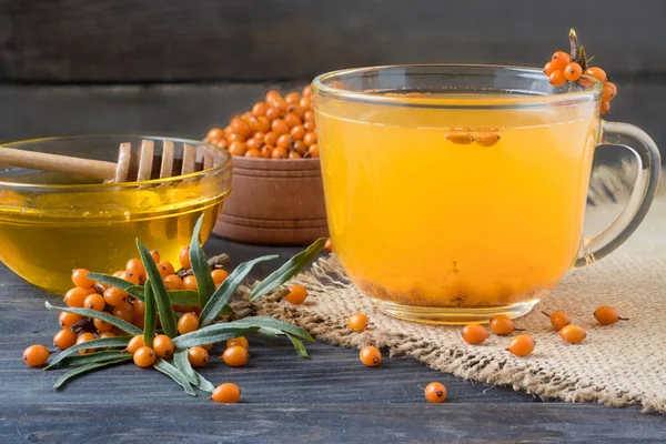 Tea of sea-buckthorn berries with a sprig on sackcloth and wooden background — Stock Photo, Image