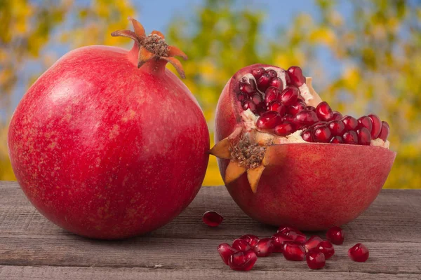 Whole pomegranate and  half on the old wooden board with blurred garden background — Stock Photo, Image