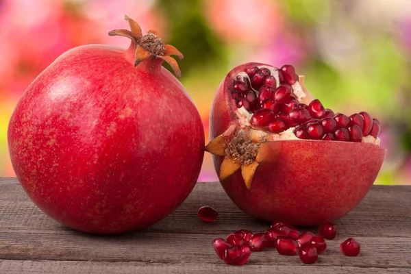 Whole pomegranate and  half on the old wooden board with blurred garden background — Stock Photo, Image