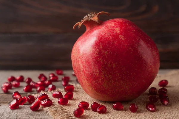 One pomegranate on the old wooden board with sackcloth — Stock Photo, Image