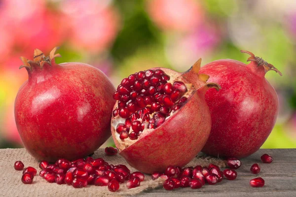 Two whole pomegranate and half on the old wooden board with blurred garden background — Stock Photo, Image