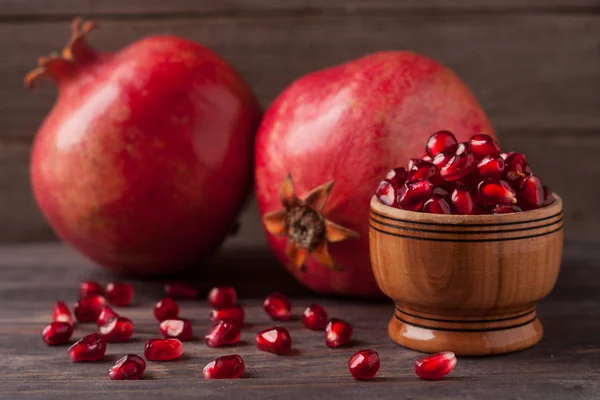 Two pomegranate and grains in the bowl on the old wooden background — Stock Photo, Image