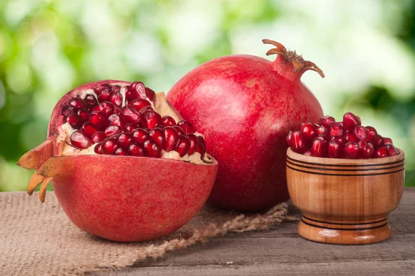 Peeled pomegranate and whole with garnet grains in a bowl on wooden background — Stock Photo, Image