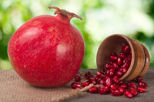 Whole pomegranate and garnet grains in a bowl on wooden background — Stock Photo, Image
