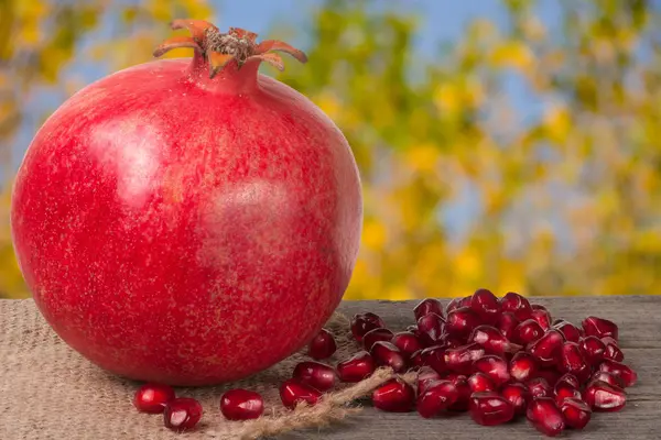 One pomegranate on the old wooden board with blurred garden background — Stock Photo, Image