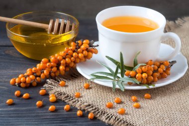 Tea of sea-buckthorn berries with a sprig on sackcloth and wooden background clipart