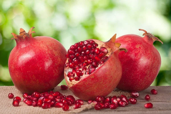 Two whole pomegranate and half on the old wooden board with blurred garden background — Stock Photo, Image