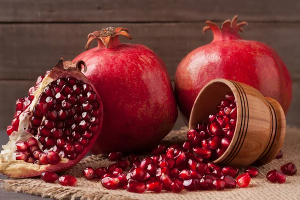 Two pomegranate and grains in the bowl on the old wooden board with sackcloth — Stock Photo, Image