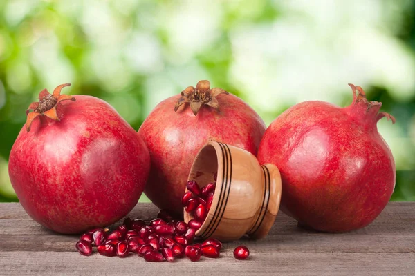 Three pomegranate and garnet grains in a bowl on wooden table with blurred garden background — Stock Photo, Image