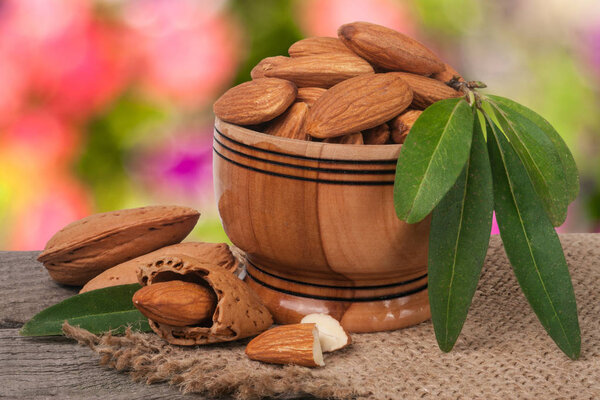 almonds in a bowl on the old wooden board with sackcloth and blurred garden background