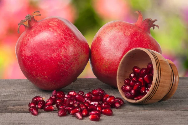 Two pomegranate and garnet grains in a bowl on wooden table with blurred garden background — Stock Photo, Image