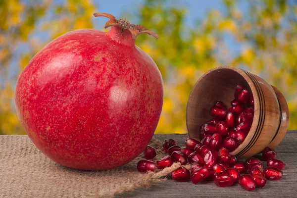 Whole pomegranate and garnet grains in a bowl on wooden background — Stock Photo, Image