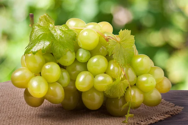 Racimo de uvas verdes maduras sobre una mesa de madera con fondo borroso — Foto de Stock