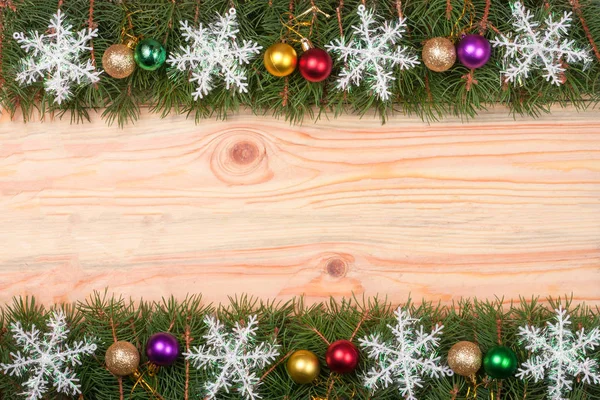 Moldura de Natal feita de ramos de abeto decorados com flocos de neve e bolas em um fundo de madeira leve — Fotografia de Stock