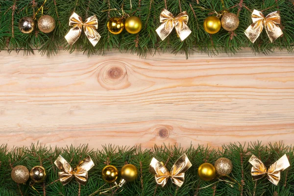 Рождественская рама из еловых ветвей, украшенных золотыми луками и шарами на светлом деревянном фоне — стоковое фото