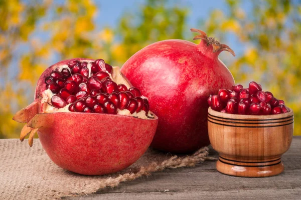 Peeled pomegranate and whole with garnet grains in a bowl on wooden background — Stock Photo, Image