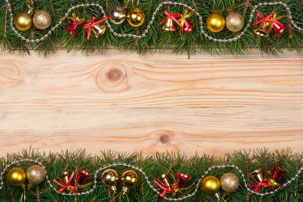 Рождественская рама из еловых ветвей, украшенных бусами и золотыми шариками на светлом деревянном фоне — стоковое фото