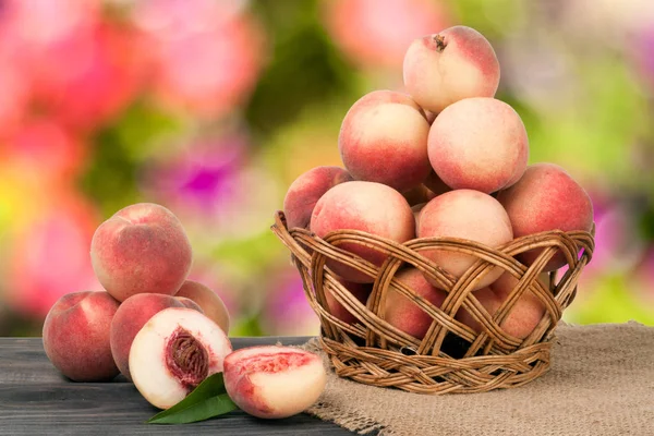Персики в плетеной корзине на деревянном столе с размытым фоном — стоковое фото