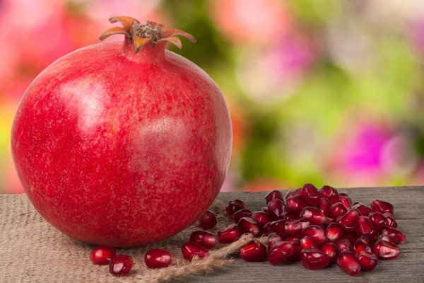One pomegranate on the old wooden board with blurred garden background — Stock Photo, Image