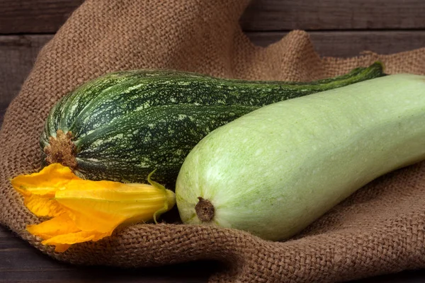 Green zucchini and courgette with a flower on sackcloth wooden background — Stock Photo, Image