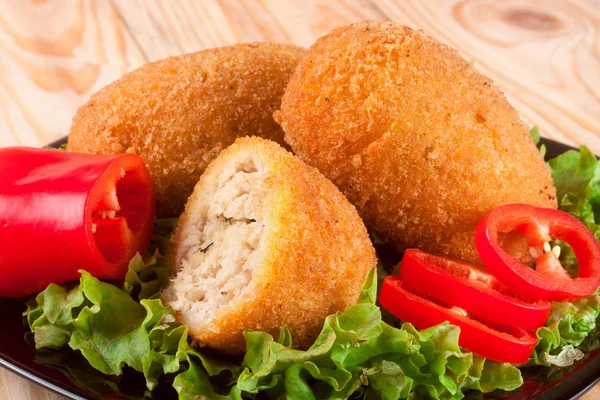 Three fried breaded cutlet with lettuce on a black plate and  wooden background — Stock Photo, Image