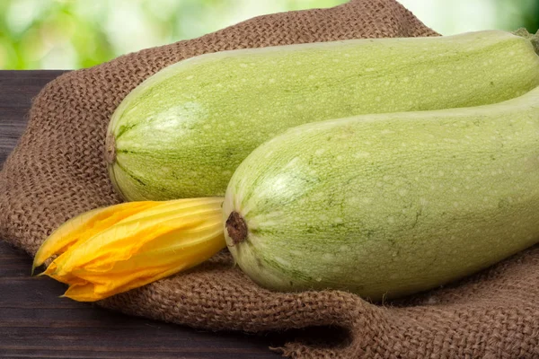 Two courgettes with a flower on sackcloth wooden background — Stock Photo, Image