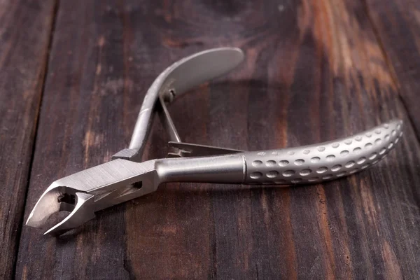 Nail clippers to remove the cuticle and care products on a dark wooden background — Stock Photo, Image