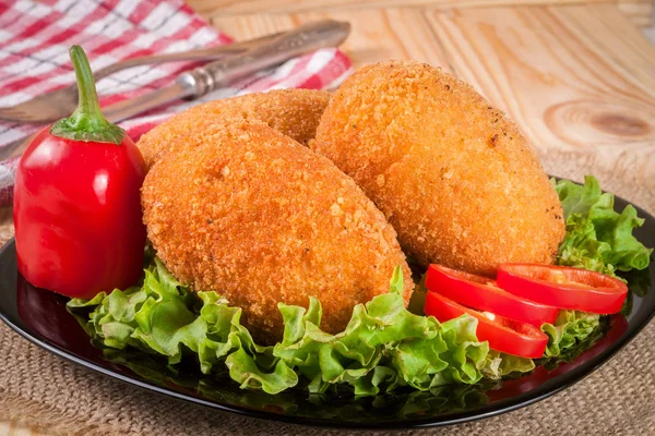 Three fried breaded cutlet with lettuce on a black plate and wooden background — Stock Photo, Image