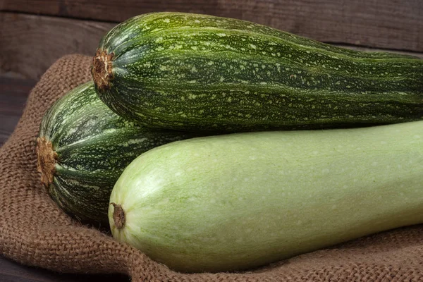 Green zucchini and courgette on sackcloth wooden background — Stock Photo, Image